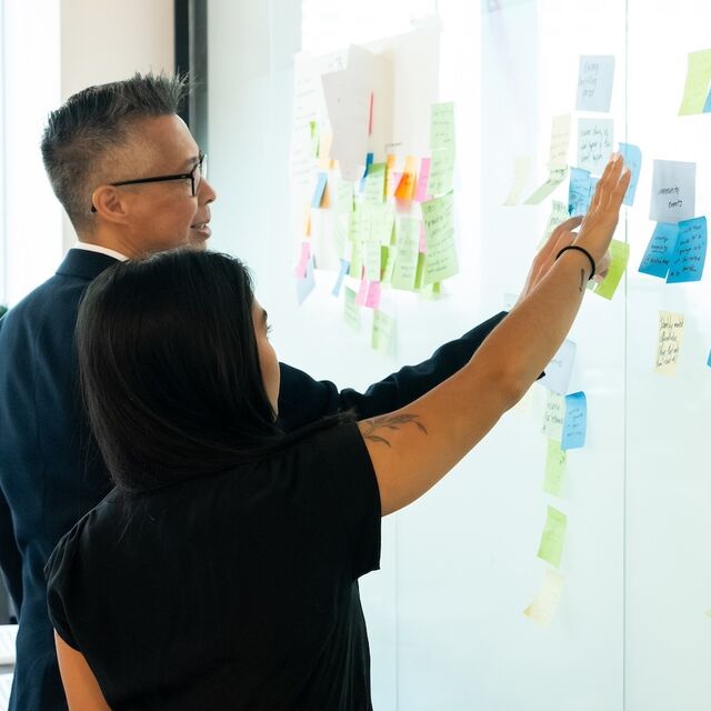 Two people looking at sticky notes on a wall