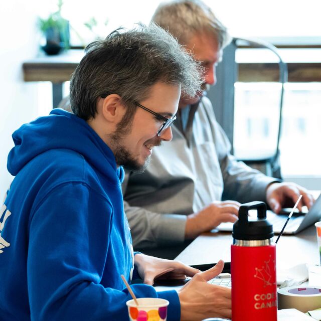 A person smiling while working on a computer next to a Code for Canada water bottle