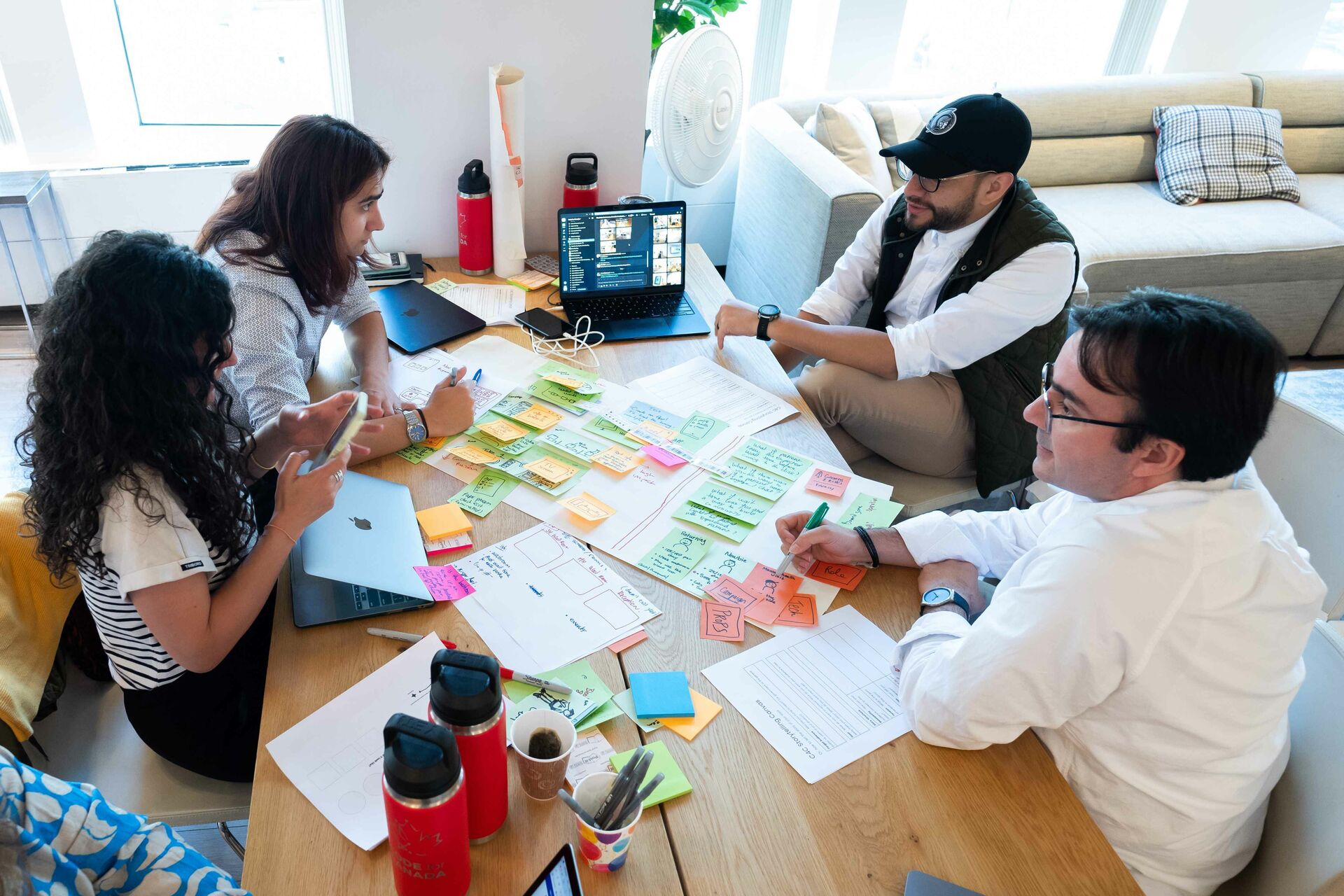 Four people sitting at a table discussing brainstorming sticky notes