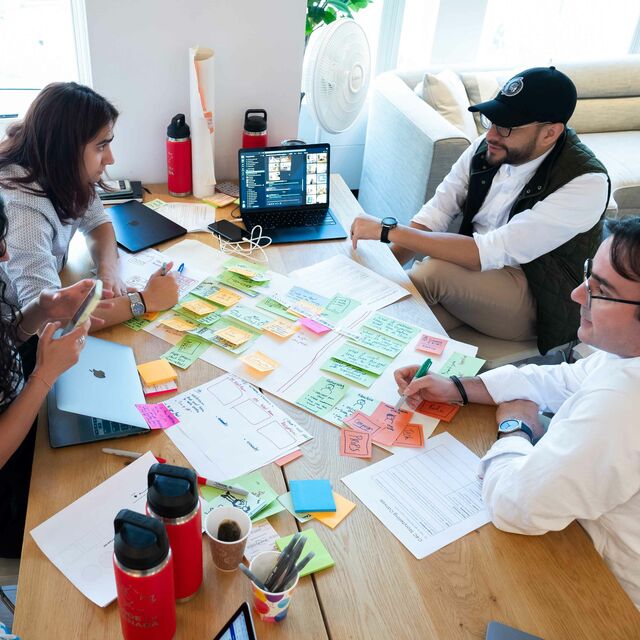 Four people sitting at a table discussing brainstorming sticky notes