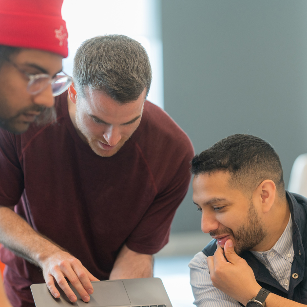 Three people gathered looking at a laptop screen