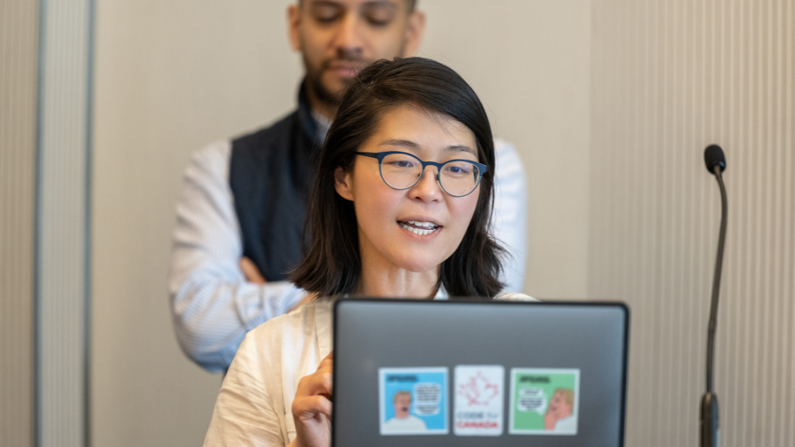 Code for Canada CEO Dorothy Eng standing at a podium in front of a laptop speaking