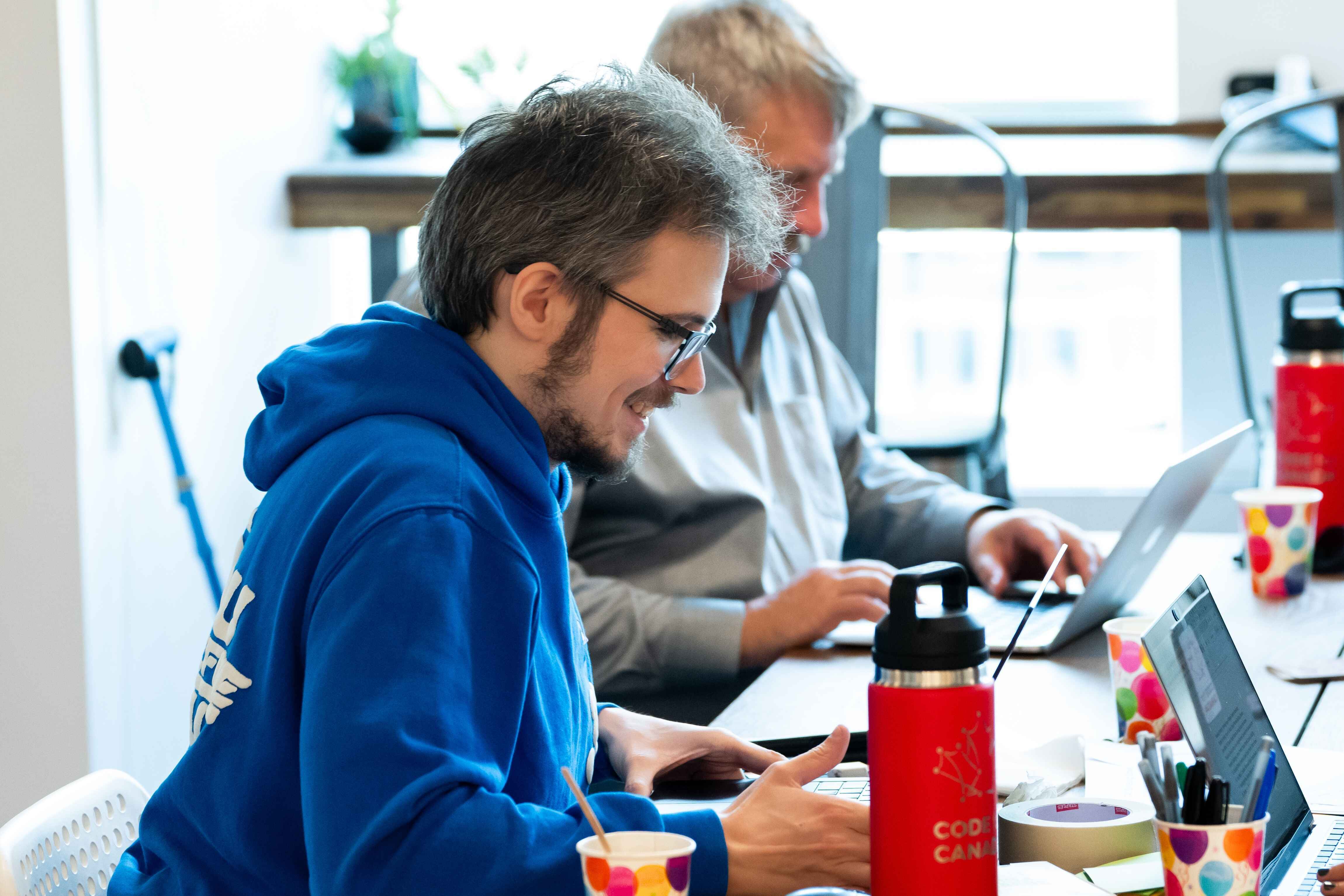 A person smiling while working on a computer next to a Code for Canada water bottle