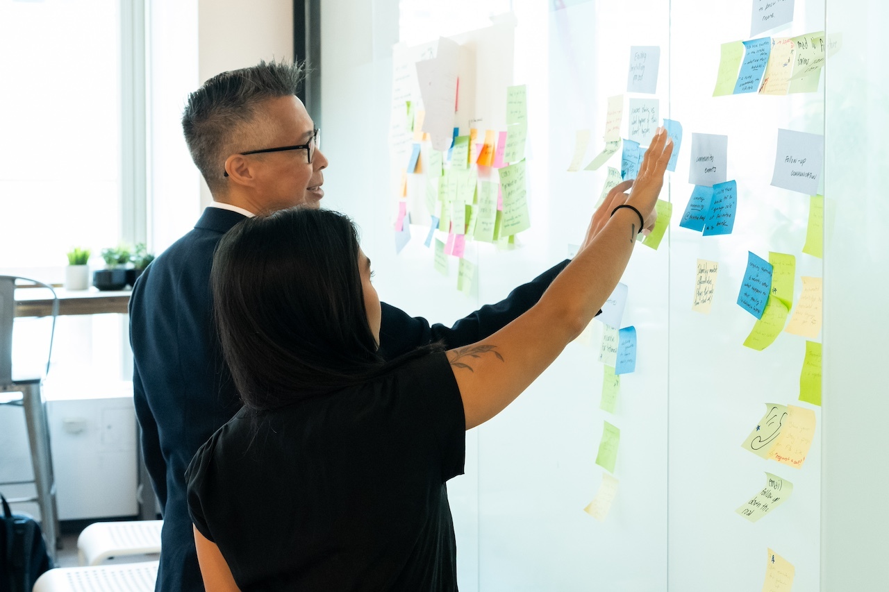 Two people looking at sticky notes on a wall